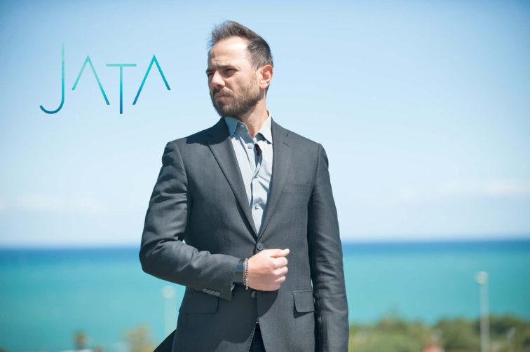 man standing outside in a suite with body of water behind him