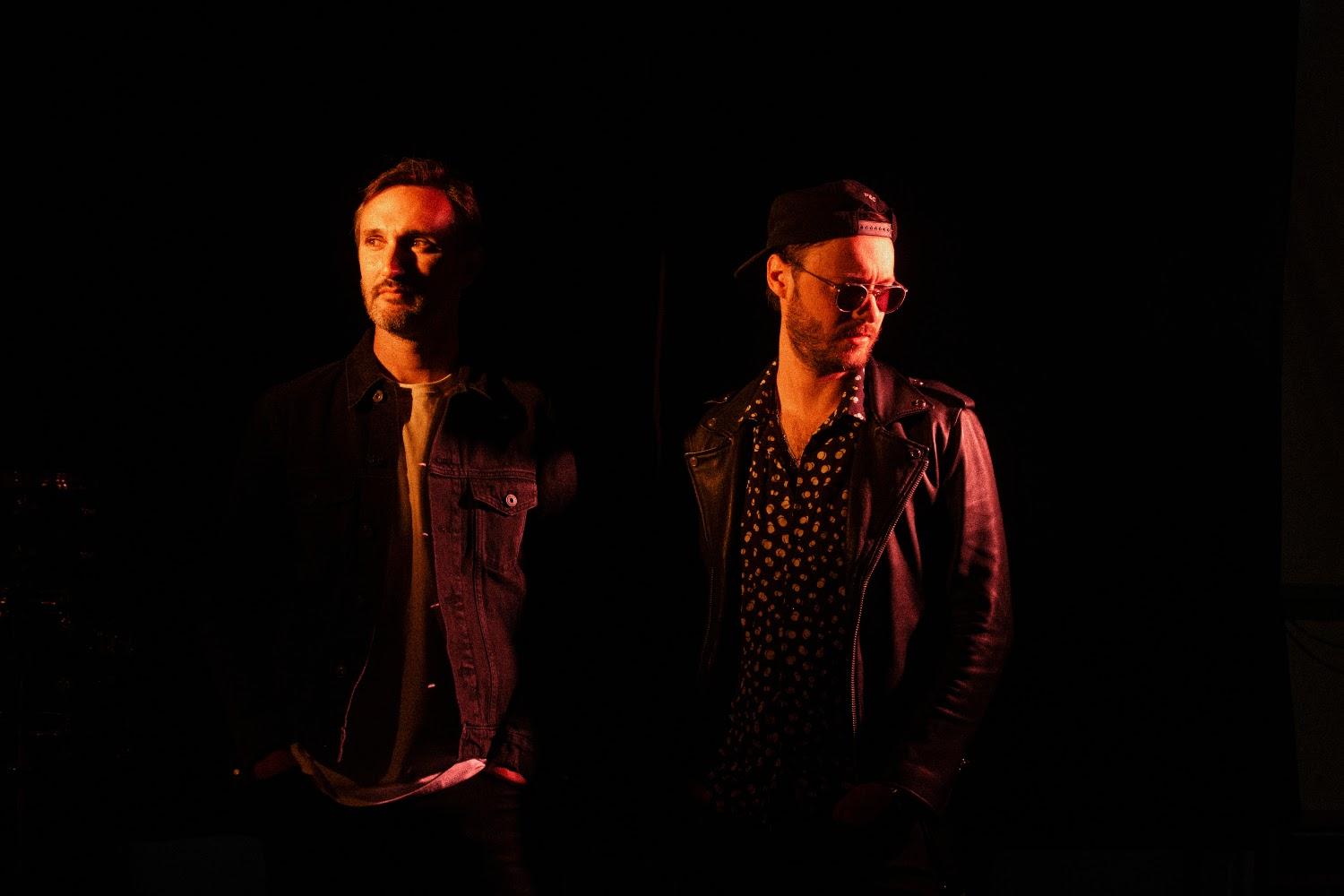 Two band members standing next to each other in a dark room with dim red lights