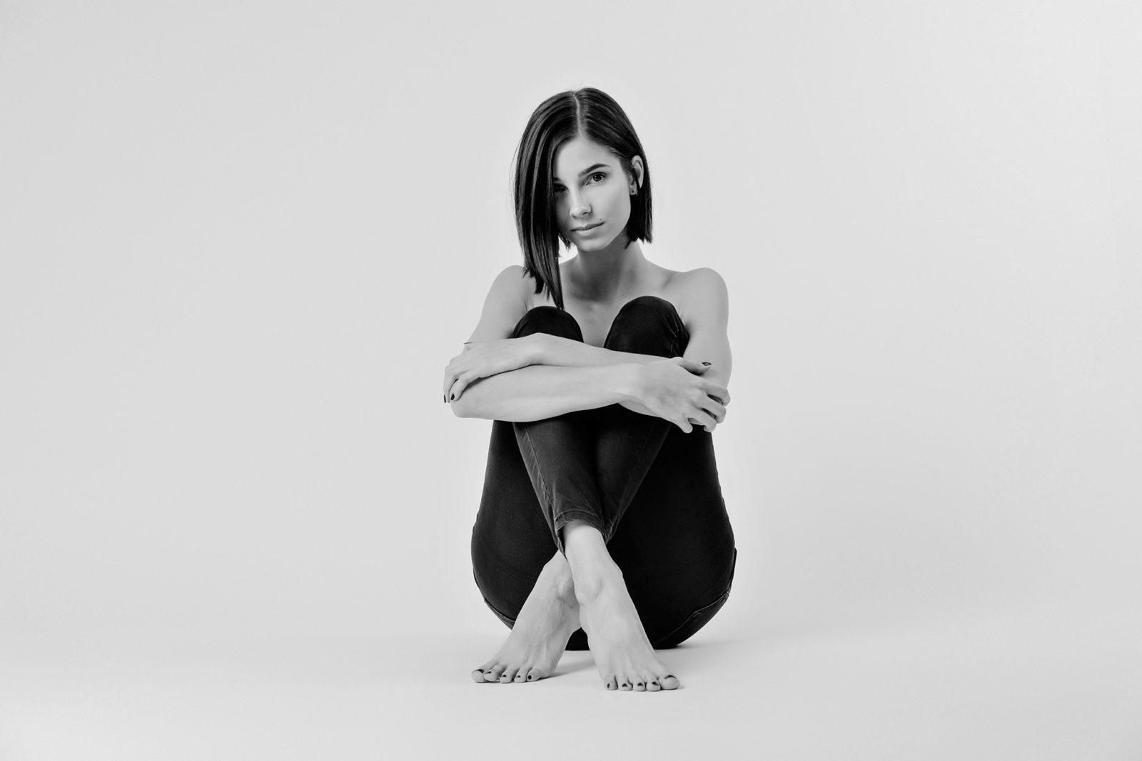 black and white photo of woman in emtpy white room, sitting on the floor