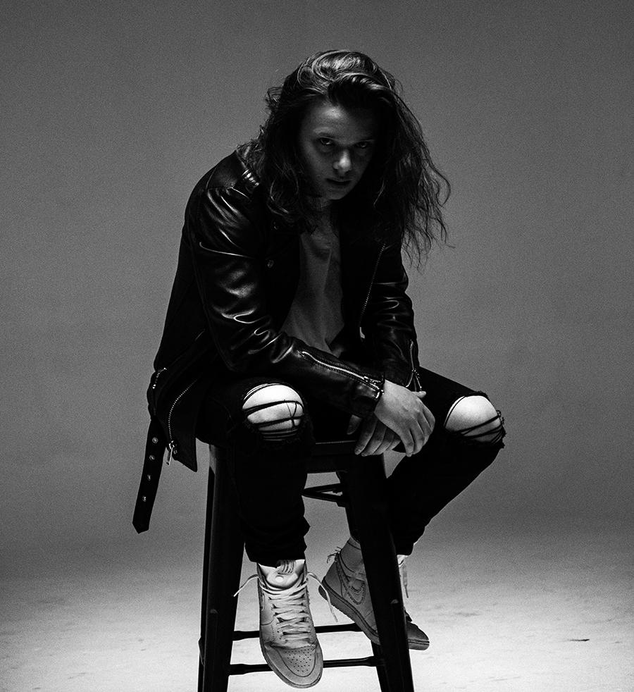 black and white photo of man in leather jacket sitting on a stool