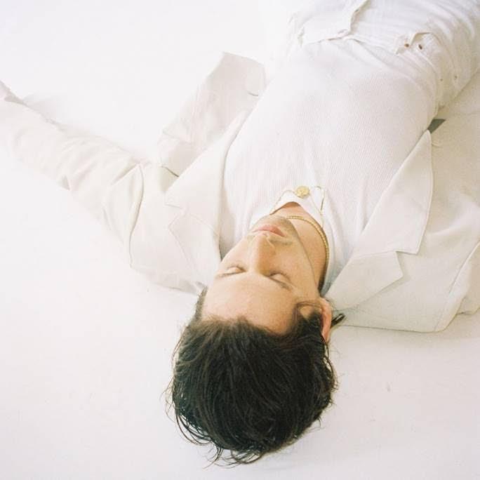 man in a white suit laying on a bed with his eyes closed