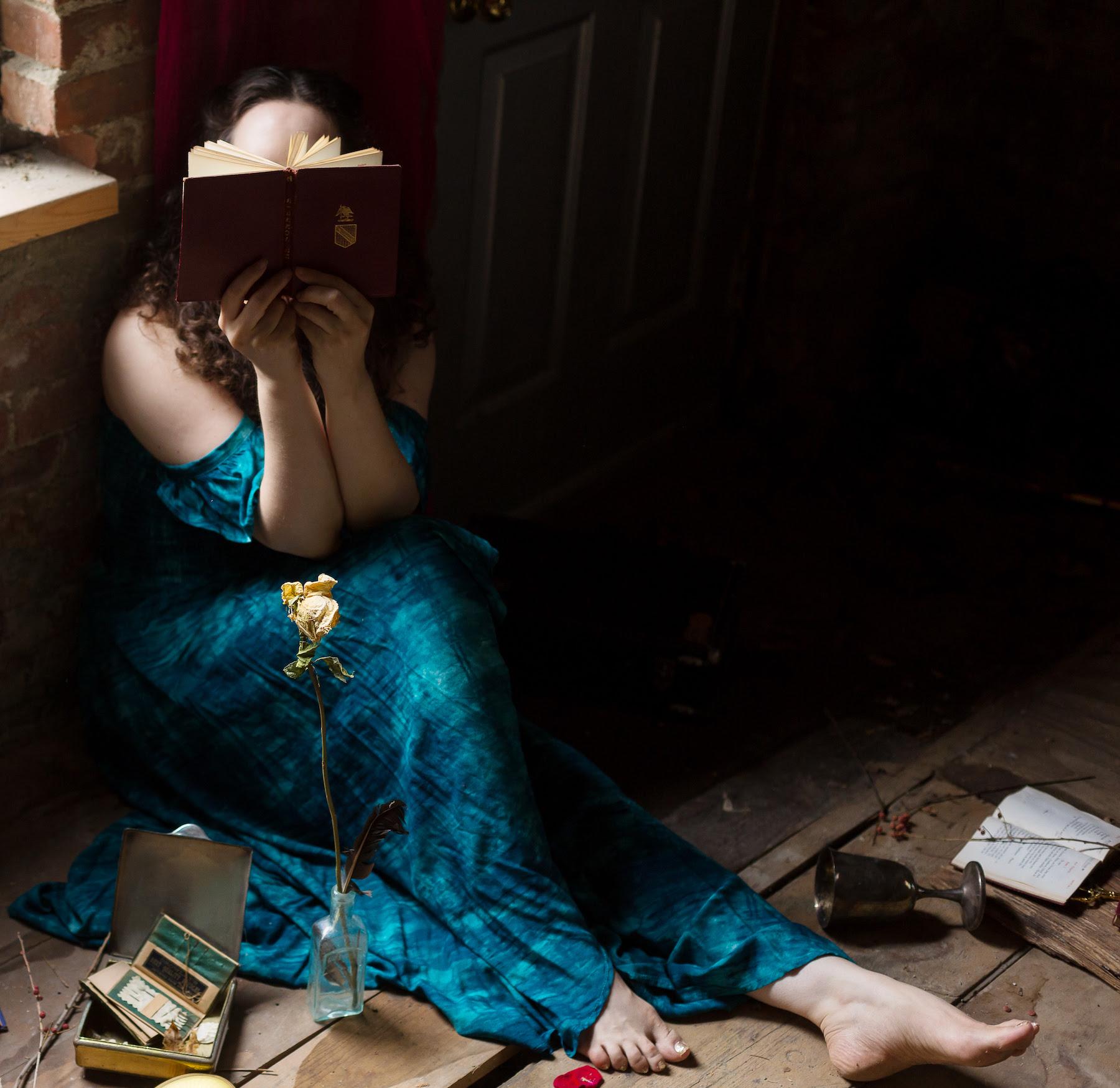 woman sitting on the floor in a dark empty room wearing a blue dress