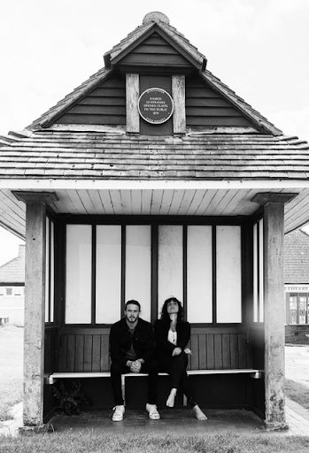 black and white image of man and woman sitting on the steps of a cottage