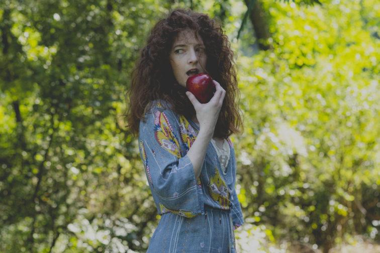 woman standin gin a forrest eating an apple