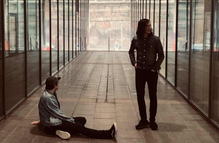 man standing in a hallway with someone sitting against the wall next to him