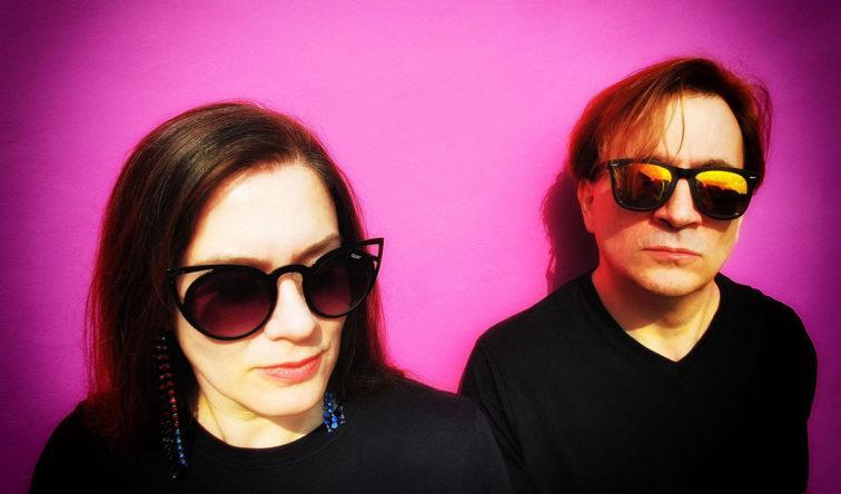 headshot of man and woman standin gin front of a blanck purple wall