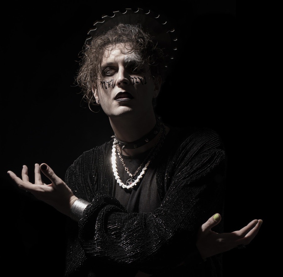 man dressed in dark goth clothing standing in a dark room