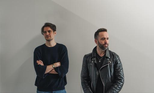 two band members standing in front of a blank wall