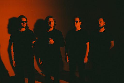 band standing in front of a blank wall with a red light shining on them