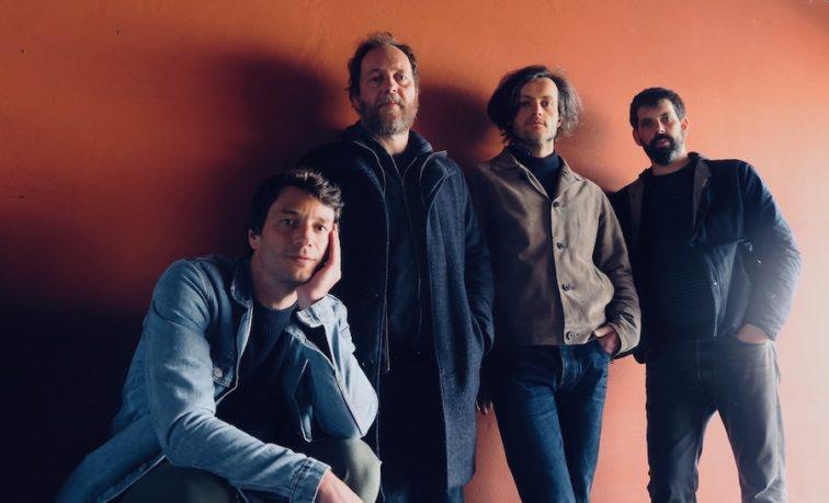 band members standing next to each other in front of an orange wall
