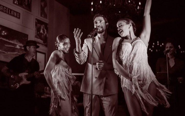 man singing on stage with two women