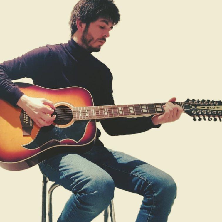 man sitting on a stool playing guitar