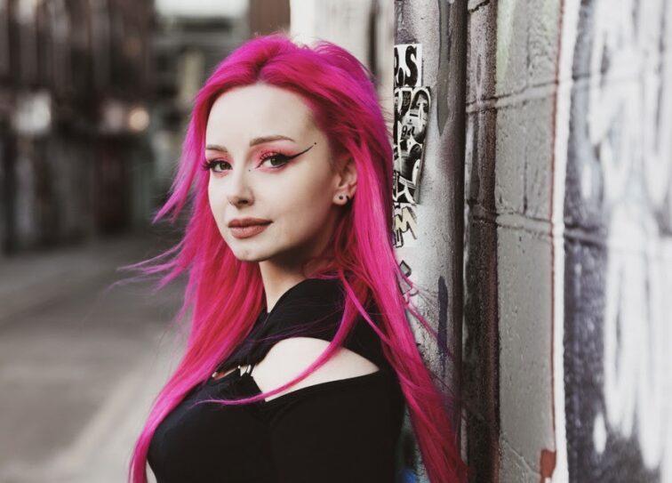 woman with pink hair standing against a wall outside