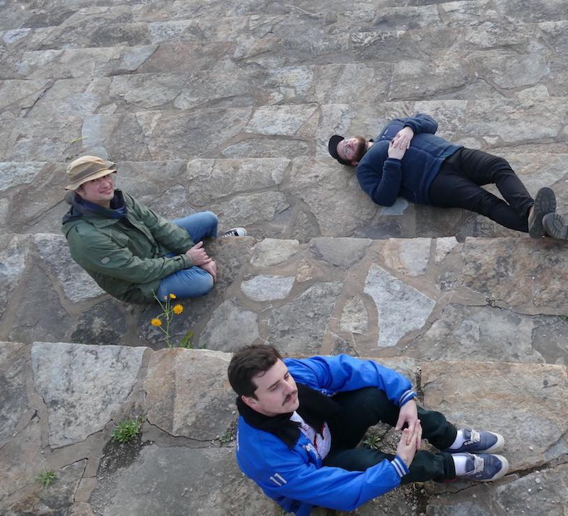 3 men sitting on a stone walkway