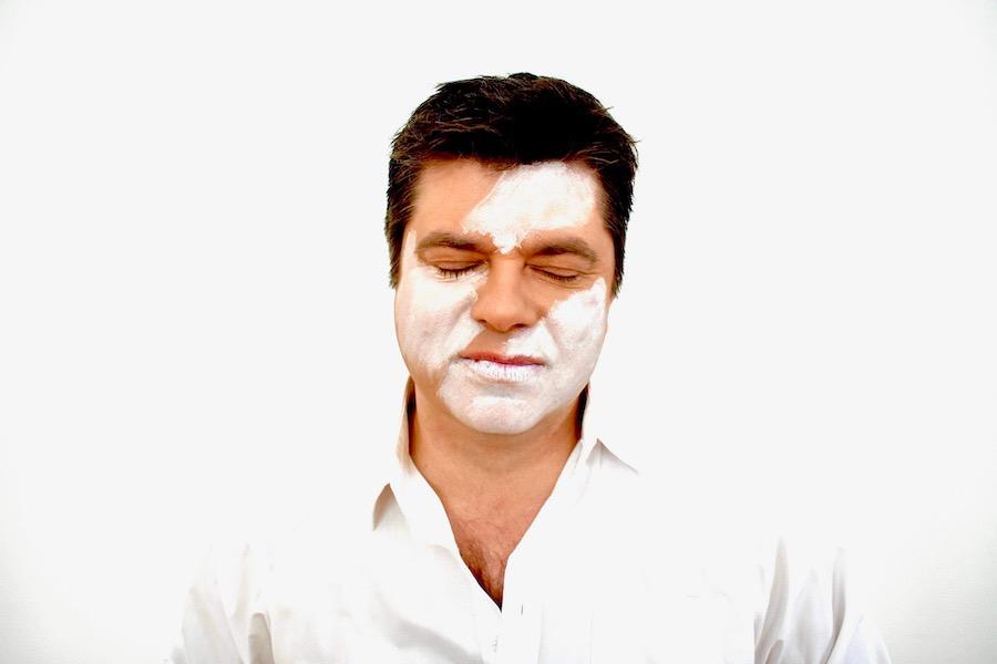 man standing with his eyes closed and half of his face painted white
