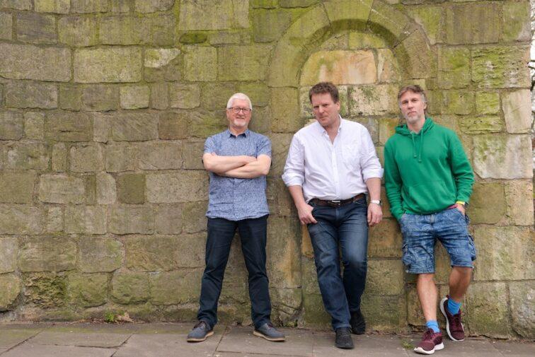 three men standing against a stone wal