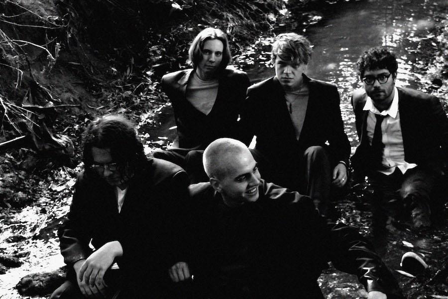 5 band members sitting by a creek in the woods