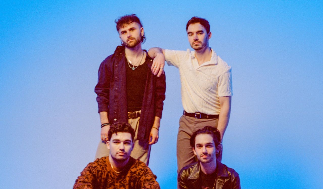 4 band members in front of a blue wall