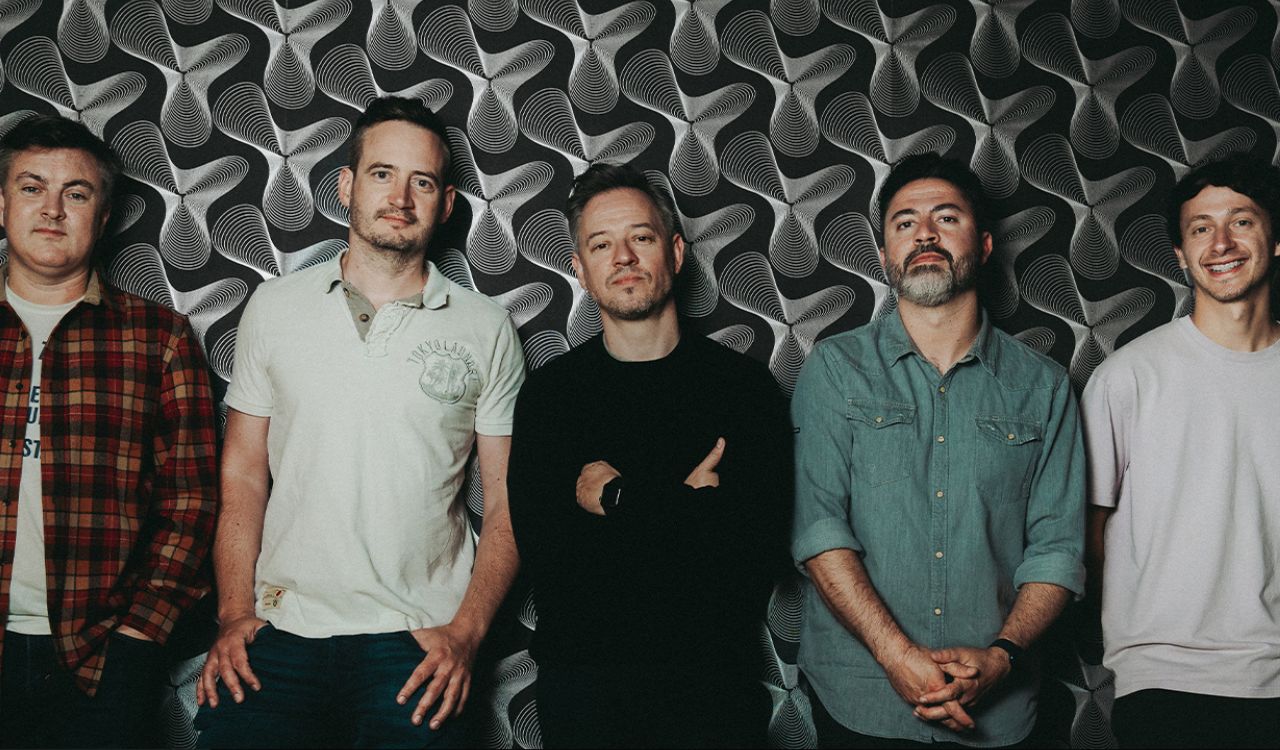 5 band members standing in front of a silver wall