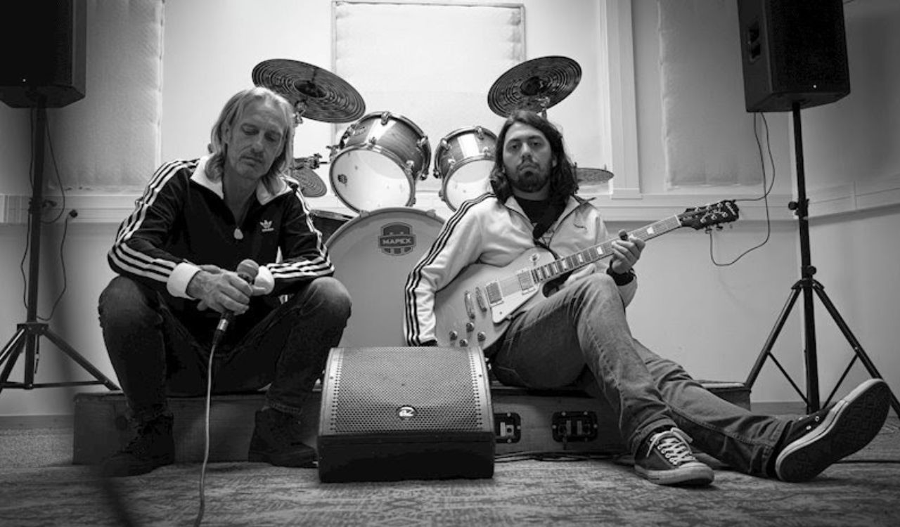 two band members sitting on the ground holding instruments