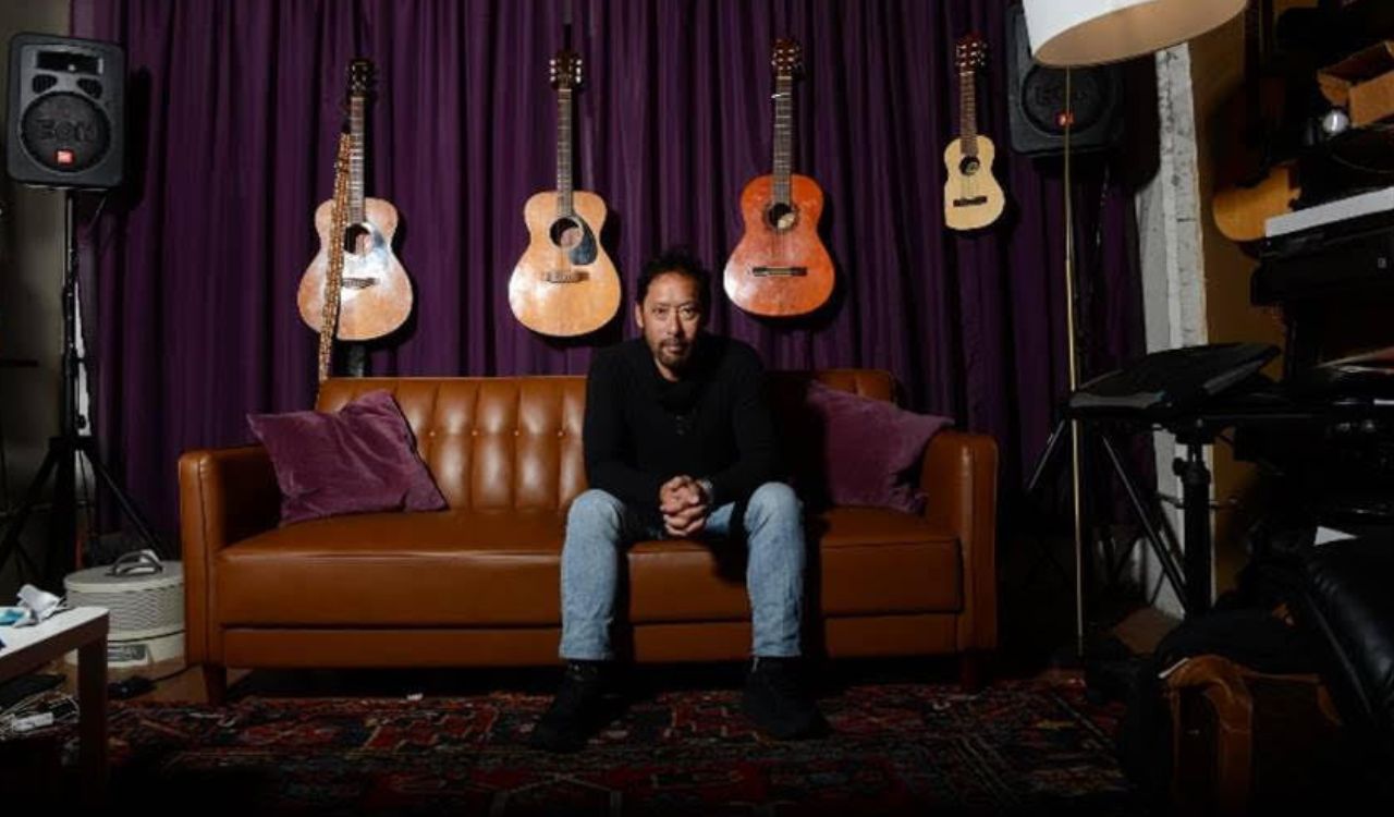 man sitting on a couch with guitars behind him