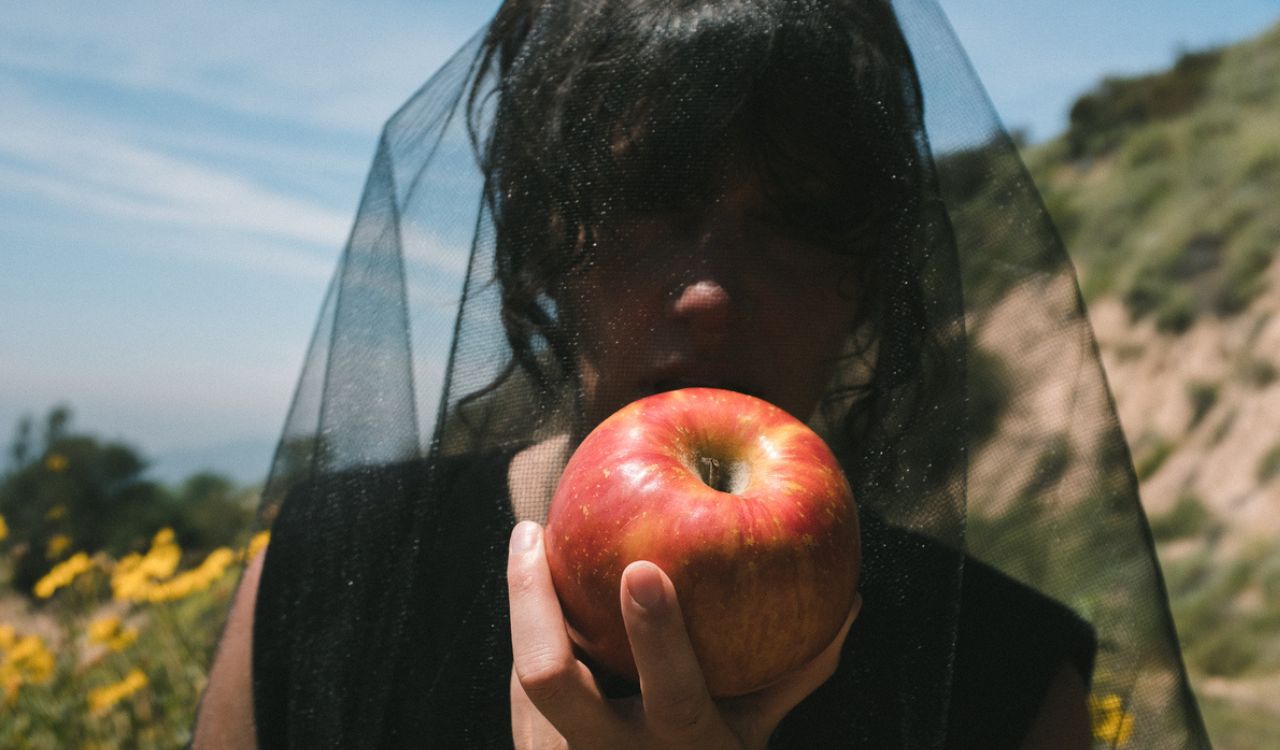 woman wearing a black veil eating an apple