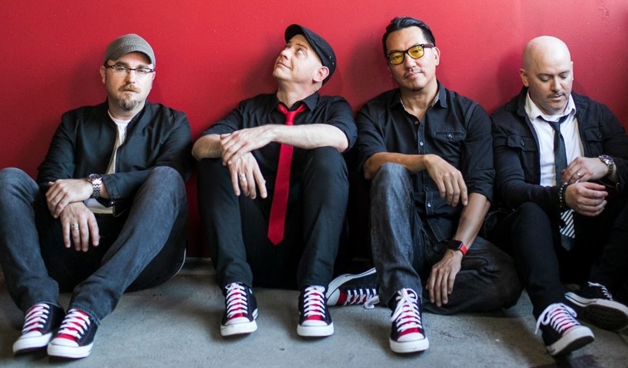 band sitting on the floor in front of a red wall
