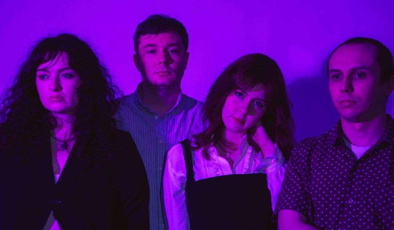band standing in front of a purple wall