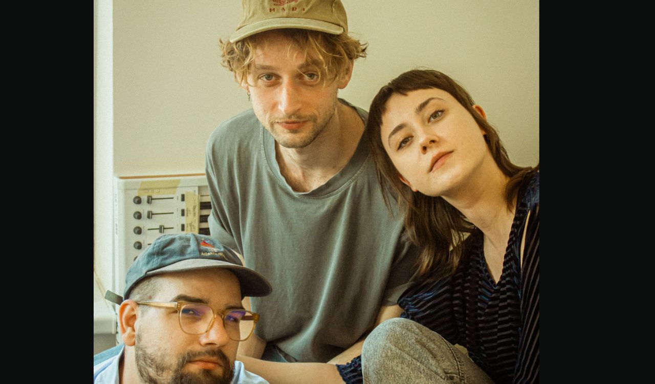 3 musicians in front of a light brown wall