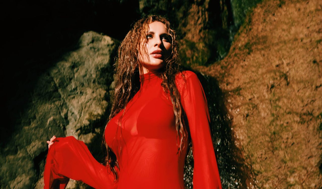woman in a red dress leaning against a big rock