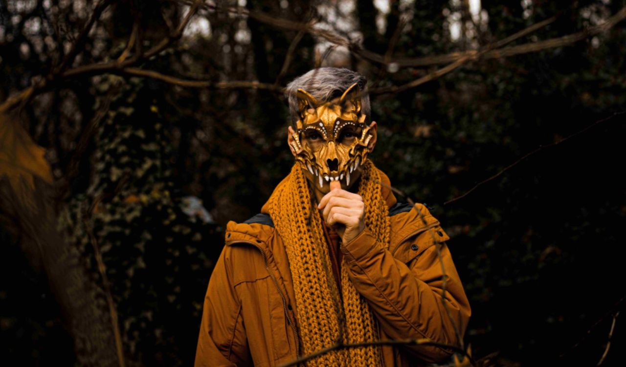 man in a dark forest holding a scary mask in front of his face