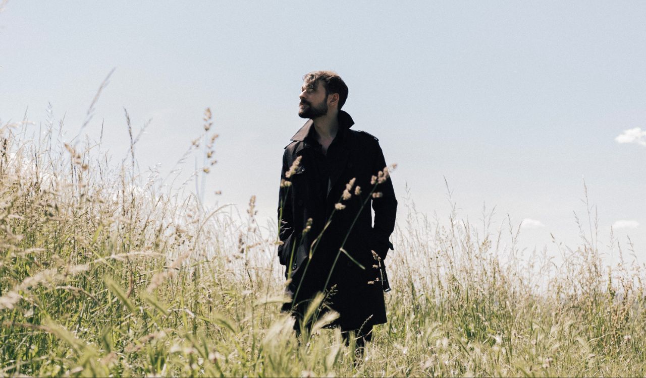 male musician standing in an open field on a sunny day