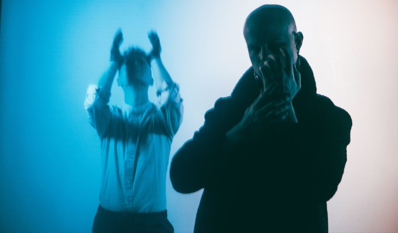 two musicians in front of a blue wall