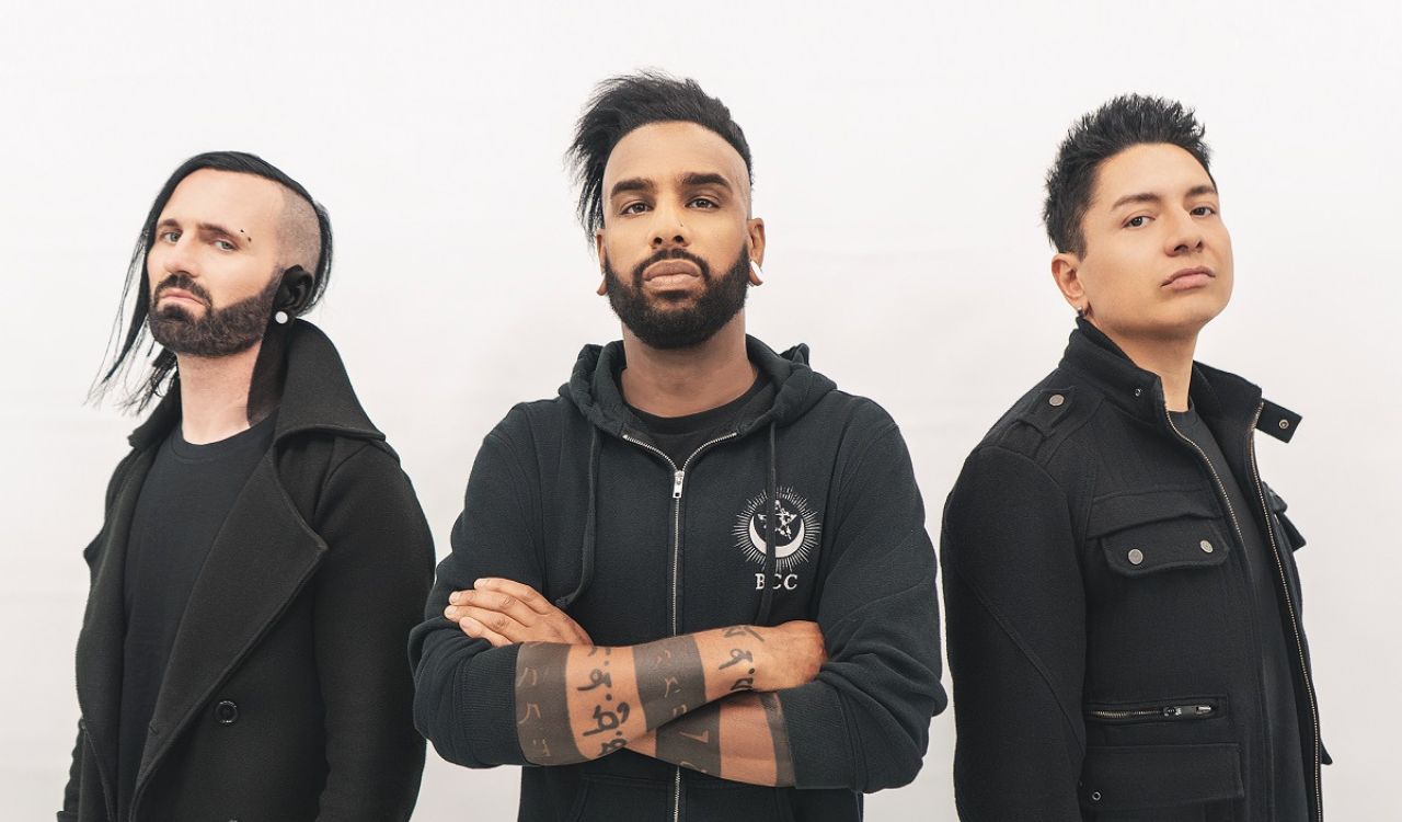 three band members standing in front of an off-white wall