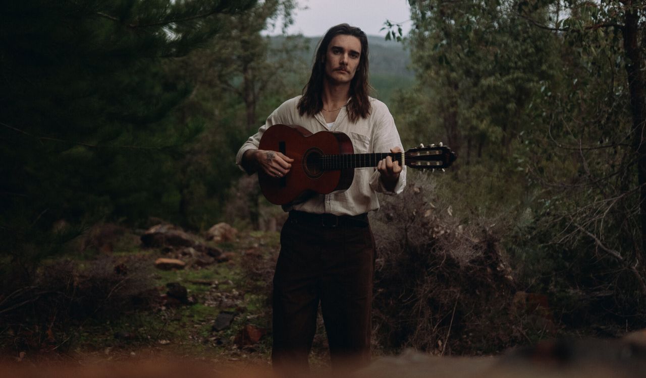 man holding a guitar in the forest