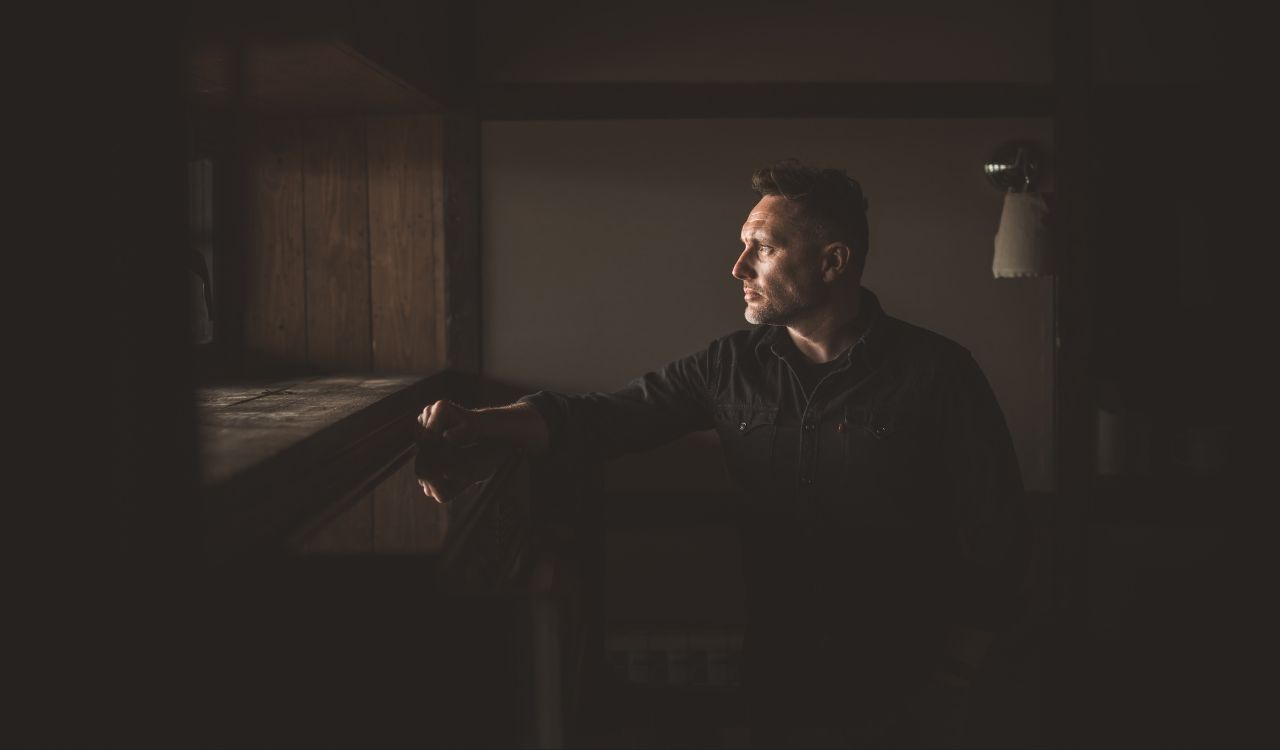 man standing in a dark room looking out a window