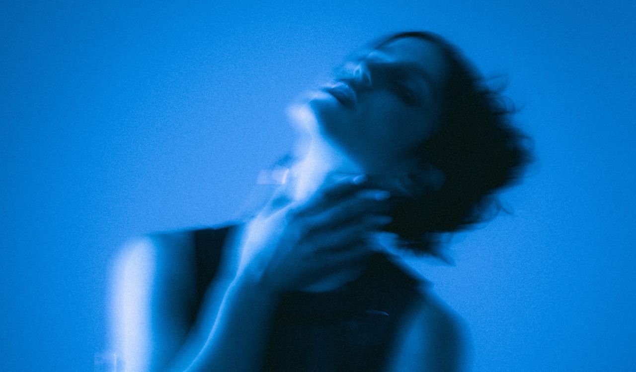 woman holding her throat in front of a blue wall