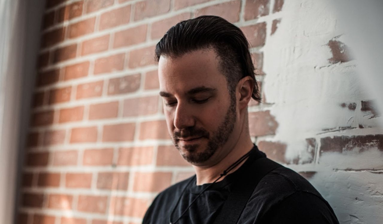 man leaning against a brick wall playing guitar