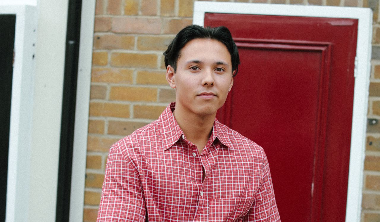 male singer standing outside in front of a red door